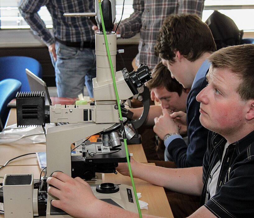 Foto (Universität Paderborn, Department Physik): Schüler des Projektkurses arbeiten an einem Lichtmikroskop, dessen Abbildung großflächig an eine Wand projiziert wird.